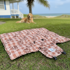 Dog lying on a patterned mat in a grassy area with a house and palm tree in the background