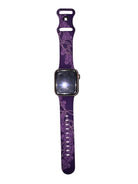 A purple smartwatch band with a floral pattern, attached to a smartwatch, displayed vertically against a plain light gray background.